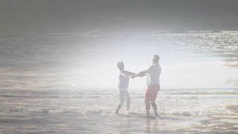 Animation-of-glowing-light-over-senior-couple-dancing-by-seaside