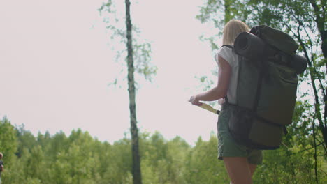 A-young-woman-with-a-map-walks-through-the-forest-traveling-with-a-backpack-in-slow-motion