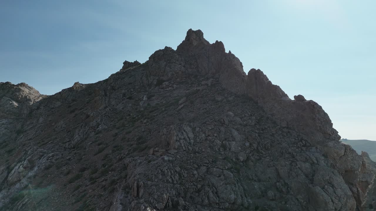 Vista aerea di una montagna rocciosa sotto un cielo sereno e una luce solare intensa.