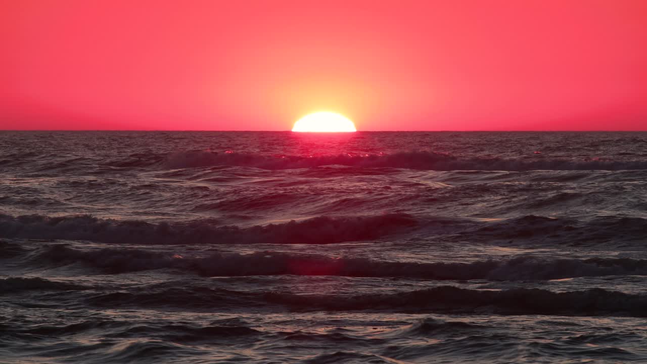 Sun setting over the sea horizon with a long focal length, radiating in a golden glow. Sunset over the sea horizon in 4K.