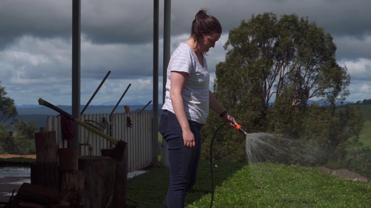 Lady water newly laid grass with hose on a farm