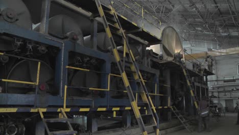 a man carries a large pile of paper over his head through a manufacturing plant