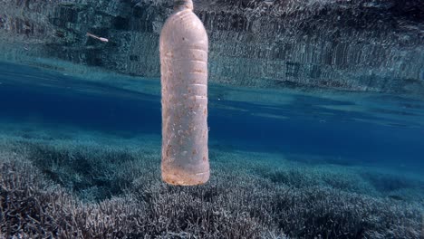 A Plastic Bottle Of Water Floating On The Blue Ocean Over The Beautiful Coral Reefs. Pollution Of The Environment. - close up shot
