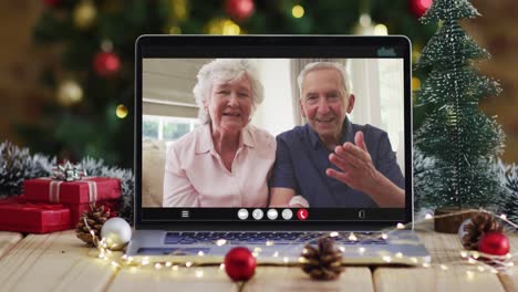 Pareja-De-Ancianos-Caucásicos-Saludando-En-Videollamada-En-Una-Computadora-Portátil,-Con-árbol-De-Navidad