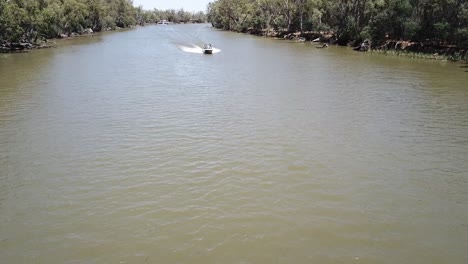 Drohnenantenne-über-Dem-Fluss-Schwenkt-Nach-Unten,-Während-Das-Boot-Vorbeirast-Und-Wellen-Schlägt