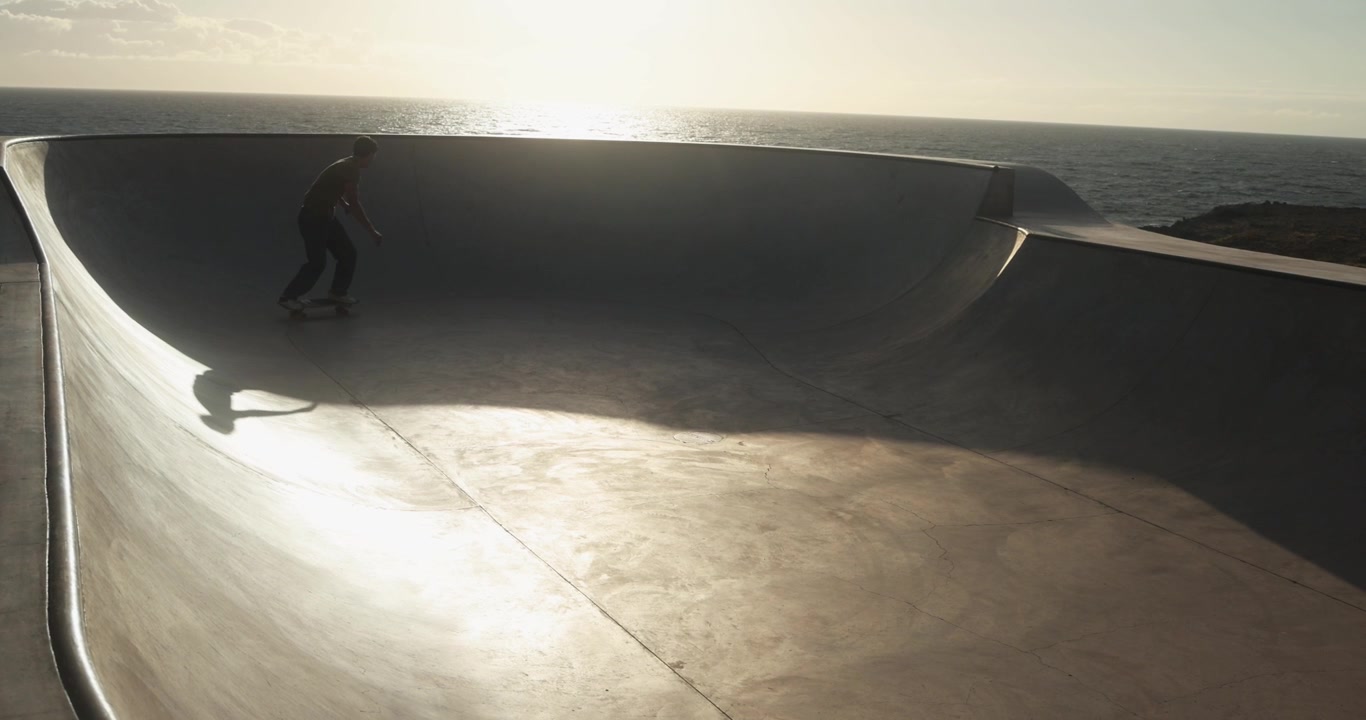 Uomo che Fa Skateboard in uno Skatepark di Cemento al Tramonto Vicino all'Oceano