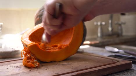 manos raspando pulpa de calabaza y semillas usando una cuchara