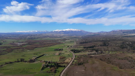 high altitude drone flyover shot in green and brown fields, with deep blue skies, some clouds and snowed mountains in back. shot on 4k-60fps