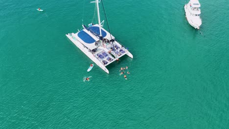 vista aérea de personas nadando alrededor de un catamarán en las aguas turquesas de phuket, mostrando una escena de vacaciones vibrante y soleada