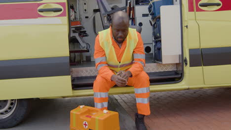 medical assistant with a first aid kit is worried and sits on the ambulance