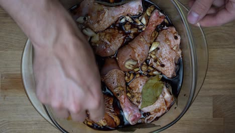 top down shot of marinating chicken pieces by hand in a glassy casserole dish