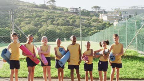 diverse group of schoolchildren standing holding mats before yoga lesson outdoors