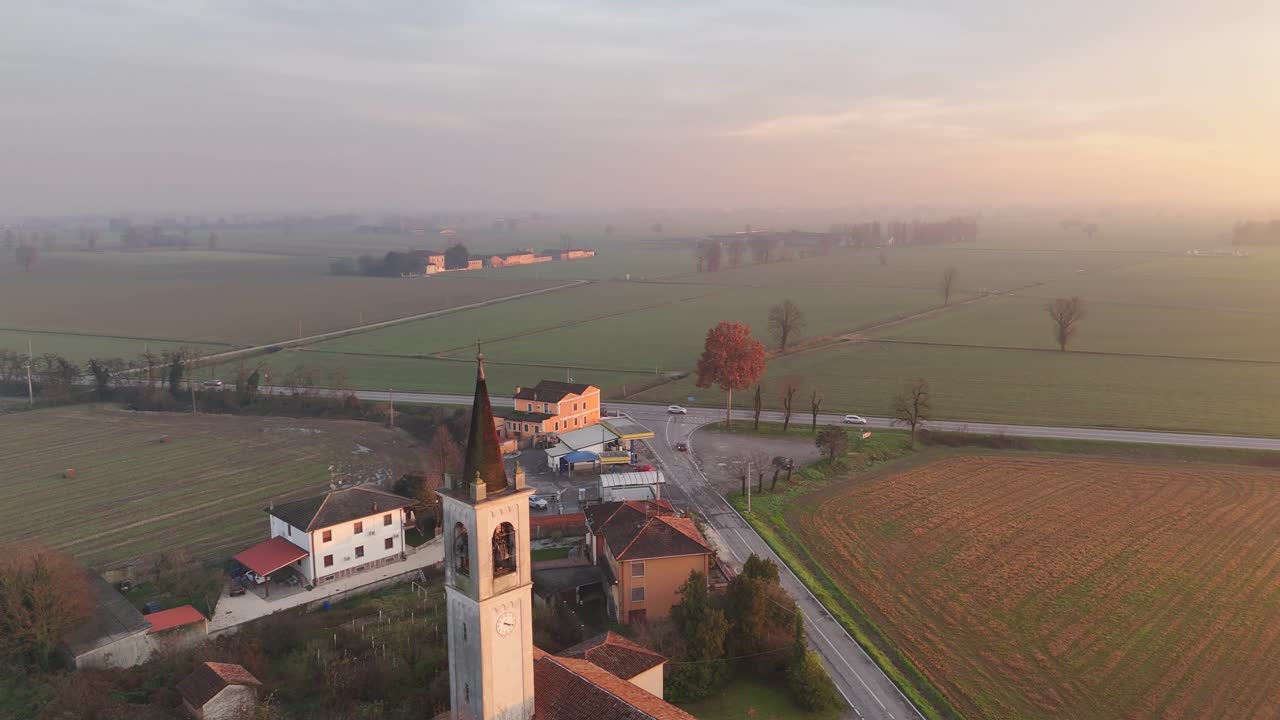 Ripresa aerea con drone in orbita elevata sopra l'insediamento di Vescovato con la torre della Chiesa di San Bartolomeo che àncora il nucleo medievale, la trattoria La Resca visibile lungo Via Mantova, la luce dorata del tramonto che illumina la campagna lombarda