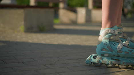 close-up side view of someone skating gently along interlocked path on rollerblades with shadows cast on ground under warm sunlight, focus on roller skates in motion