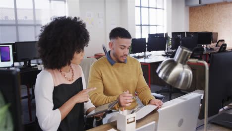 Diverse-male-and-female-colleagues-at-desk-using-tablet,-making-notes-and-talking,-slow-motion