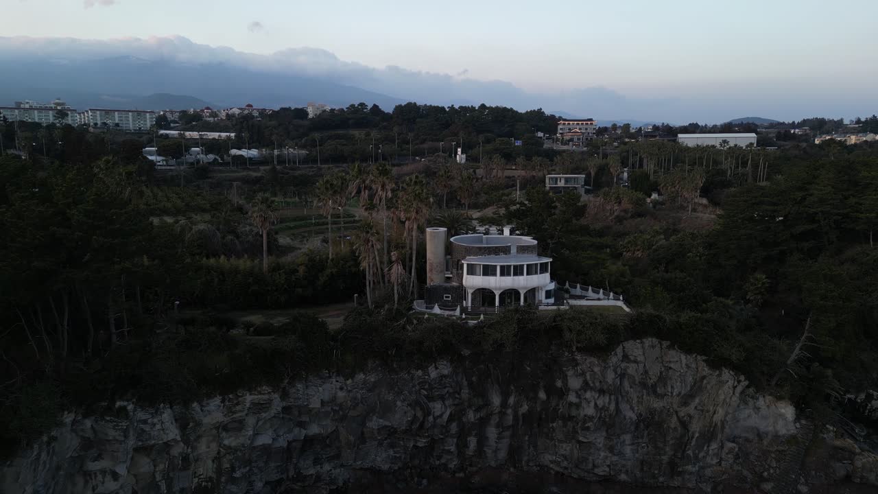 Drone aerial view in South Korea near a cliff with green trees over rocky area sunset jeju island