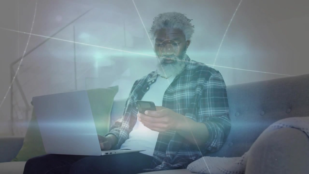 Noticing overlay graphics, middle-aged man scrolling smartphone on couch laptop open in plaid shirt