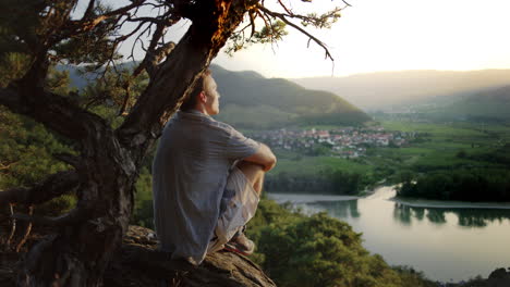 Hombre-Mirando-La-Puesta-De-Sol-Debajo-De-Un-árbol,-Fondo-De-Paisaje-De-Montaña,-Hora-Dorada-Del-Valle-Del-Danubio,-Descripción-General,-Mirando-Hacia-Afuera,-Pacífico,-Desintoxicación,-Desintoxicación-Digital,-Naturaleza-Al-Aire-Libre,-Desintoxicación