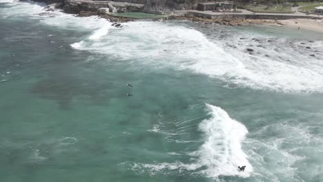 La-Gente-En-Sus-Tablas-De-Surf-Está-A-La-Deriva-Rompiendo-Olas-En-La-Playa-Bronte-Con-Baños-Bronte-En-Sydney,-Australia