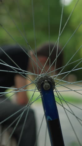 primer plano de la rueda giratoria de la bicicleta en foco, creando un efecto borroso de una persona sentada en un banco con la cabeza inclinada hacia abajo, el fondo, incluida la figura y el paisaje, está borroso