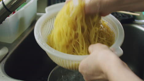 korean mother washing and cooling down jjolmyeon korean noodles after boiling in a colander