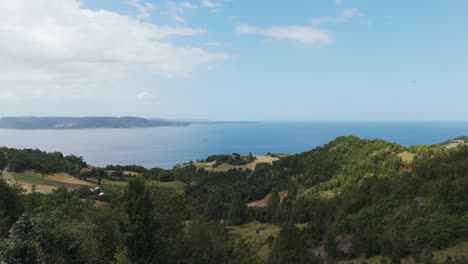 closed parasols shading a wooden bench overlooking reloncavi sound and the green hills of lemuy island, chile, on a beautiful sunny day. aerial dolly forward