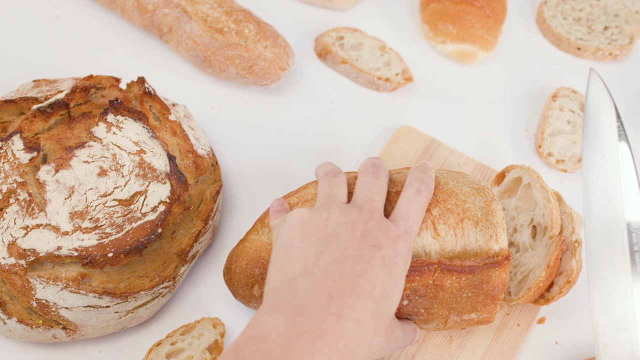 Overhead view of hands using a knife to slice crusty sourdough bread on white background.