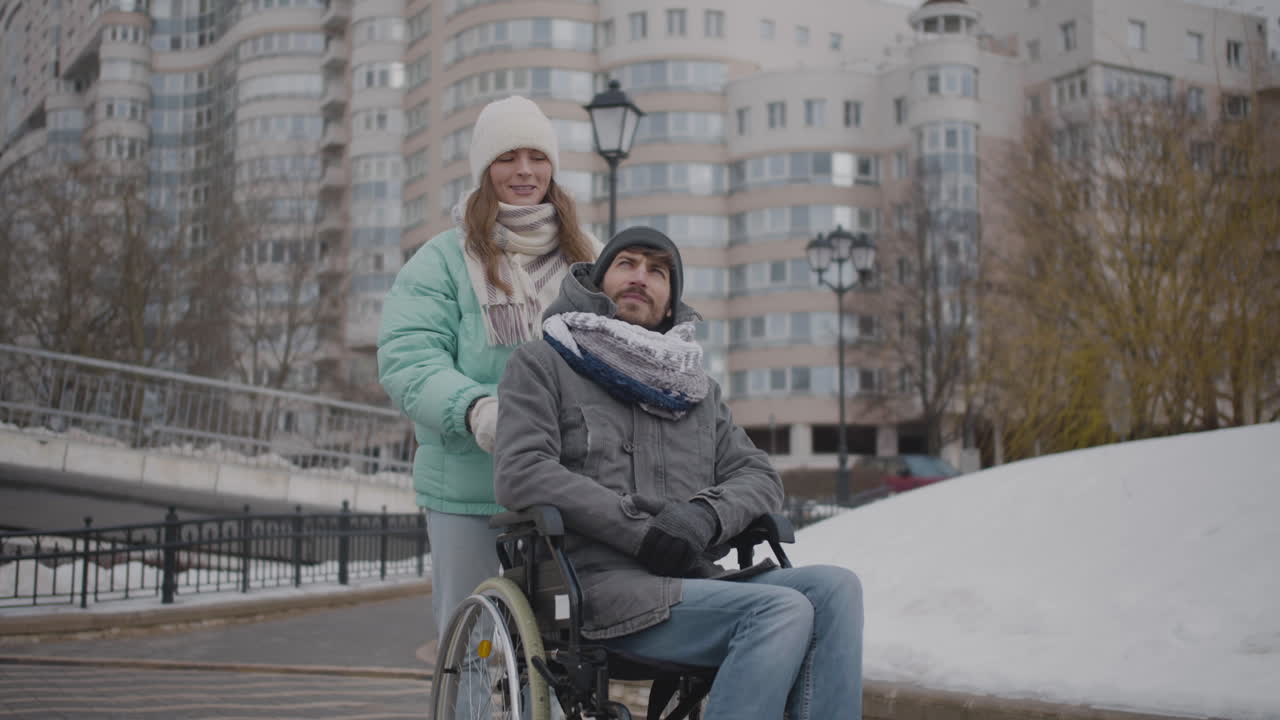 Happy Caucasian woman taking her disabled friend in wheelchair for a walk in the city and looking at something interesting in the sky