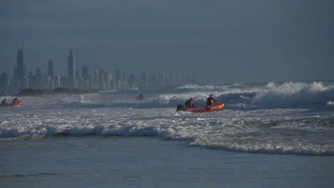 Australian-Volunteer-Lifeguards-On-Duty---Surf-Lifesaving-team-Riding-Rough-Waves-In-An-Inflatable-Rubber-Boat---Gold-Coast-Skyline-From-Currumbin-Beach,-Queensland,-Australia