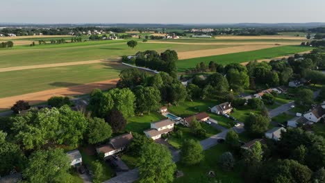 quaint and quiet suburb neighborhood near rural farm fields during golden sunset in america. aerial flyover shot. neatly arranged homes, lush green lawns and winding streets. top down