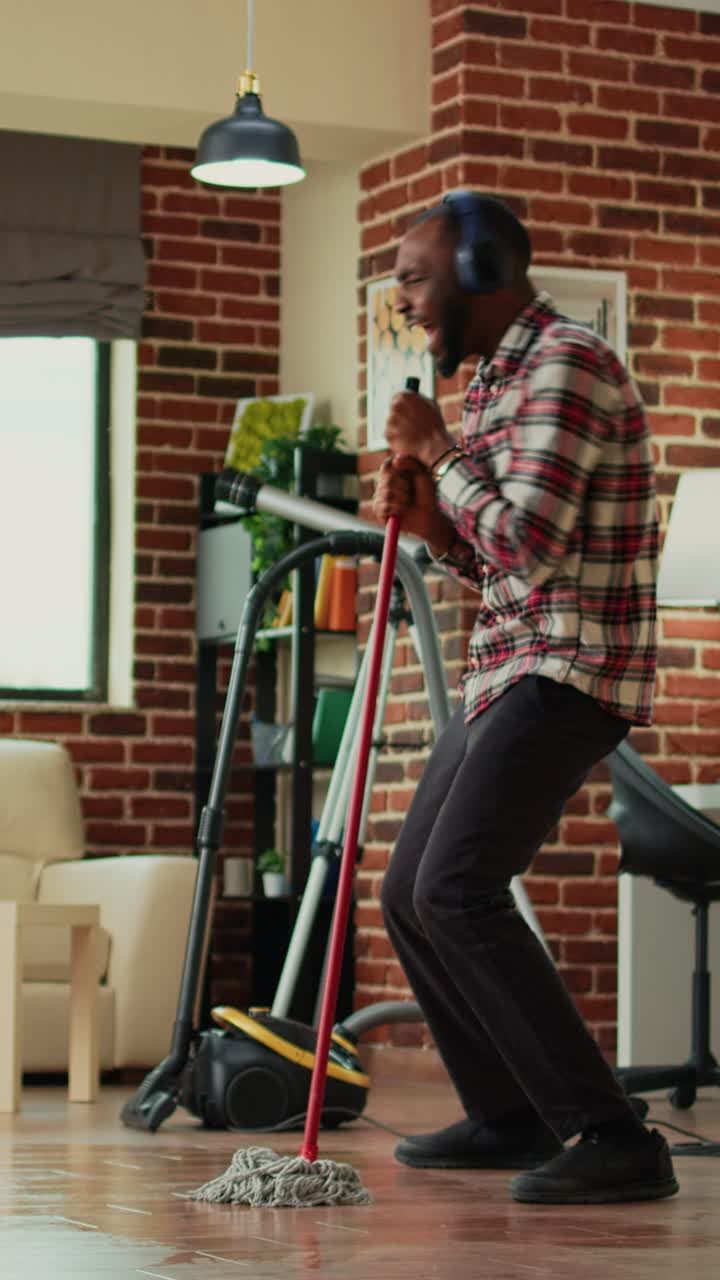 Vertical video: Young male adult having fun with mop and music at home