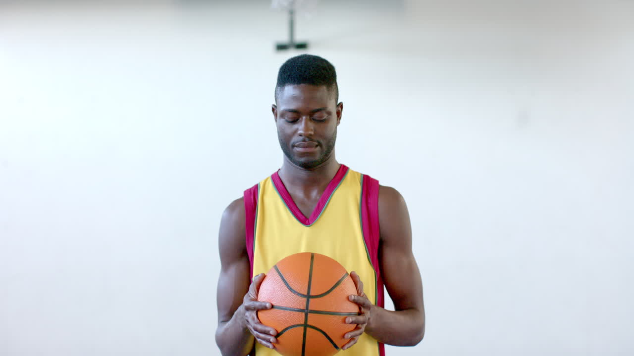 hombre afroamericano enfocado sosteniendo una pelota de baloncesto en la cancha