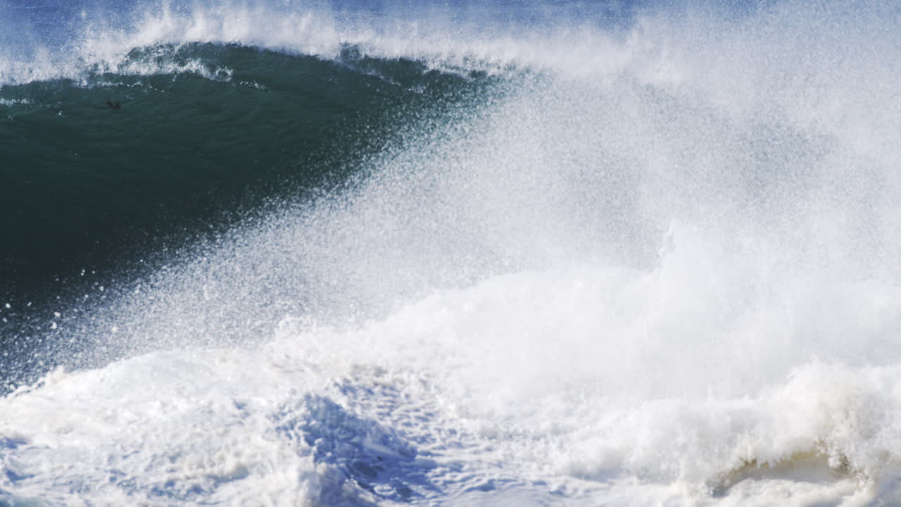 Towering white wave crashes with textured mist lifting above in super slow motion