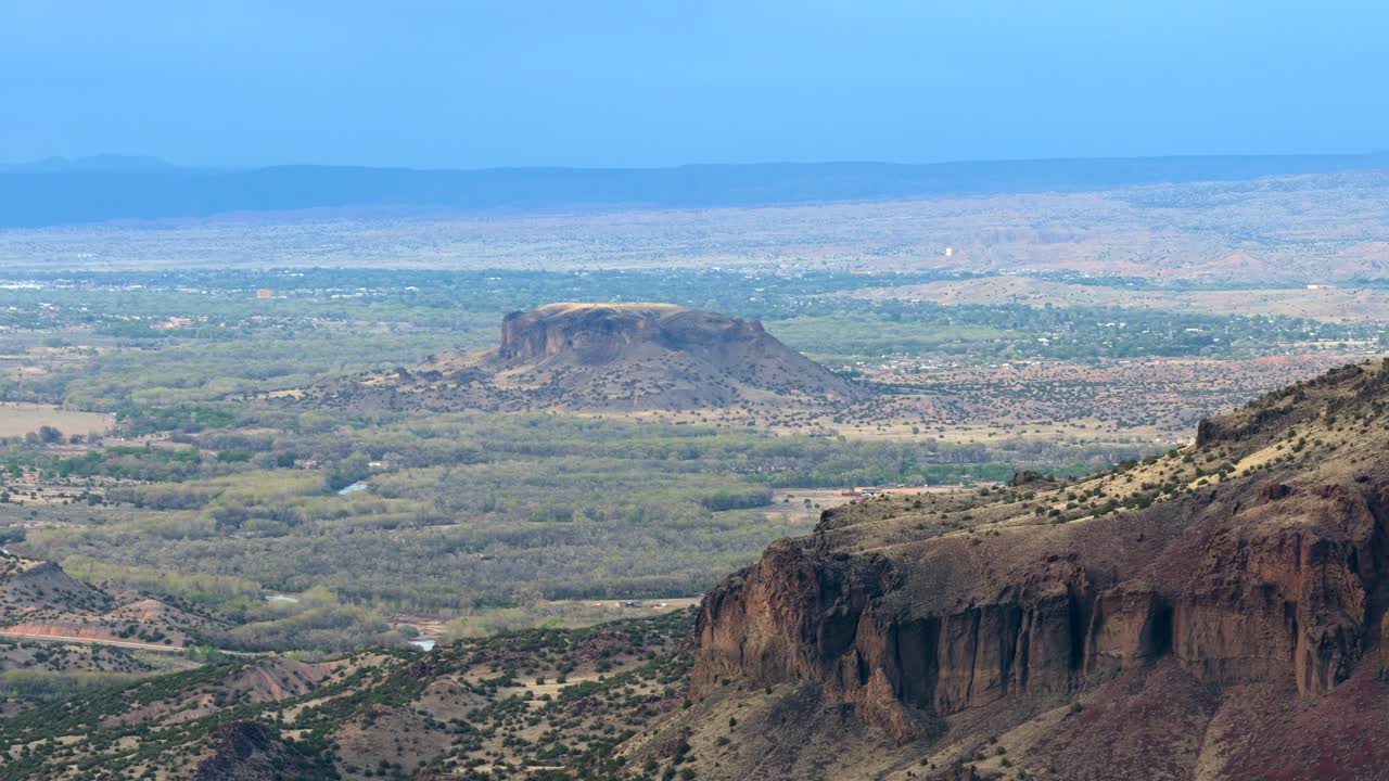 Una ripresa cinematografica con drone cattura un drammatico paesaggio di canyon del Sud-Ovest. L'iconica Black Mesa si erge su un terreno desertico dai colori tenui e vasti panorami aridi