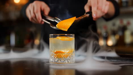 bartender preparing and flaming an orange peel garnish for a cocktail with dry ice