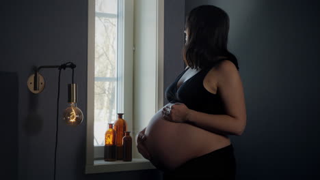 Portrait-of-beautiful-pregnant-woman-in-bra-standing-by-window