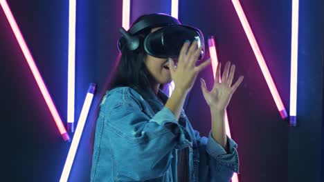 young woman playing and smiling  in the vr headset. virtual reality helmet on color lighting background