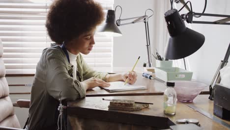 trabalhadora biracial ocupada desenhando design de jóias em estúdio de jóias em câmera lenta