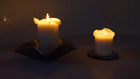 Still-shot-of-two-lit-candles,-one-large-one-small,-in-a-dark-room