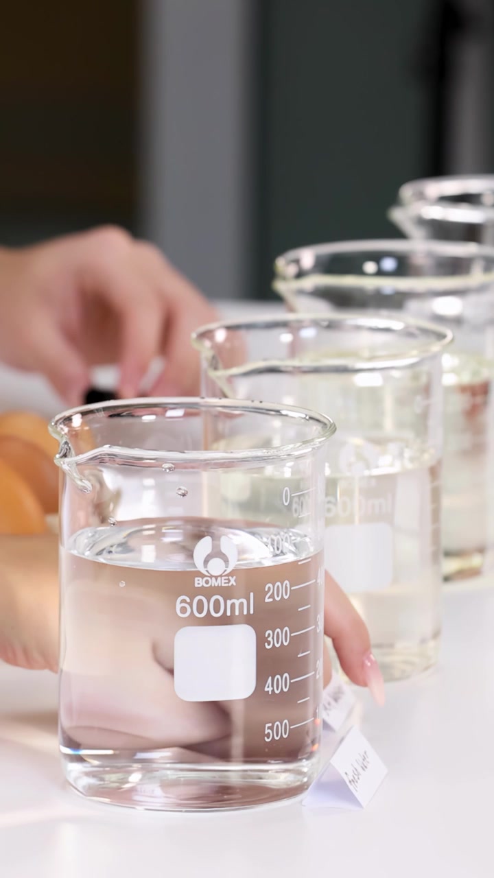 Primo piano delle mani che lasciano cadere un uovo in un becher pieno d'acqua per un esperimento di chimica scolastico