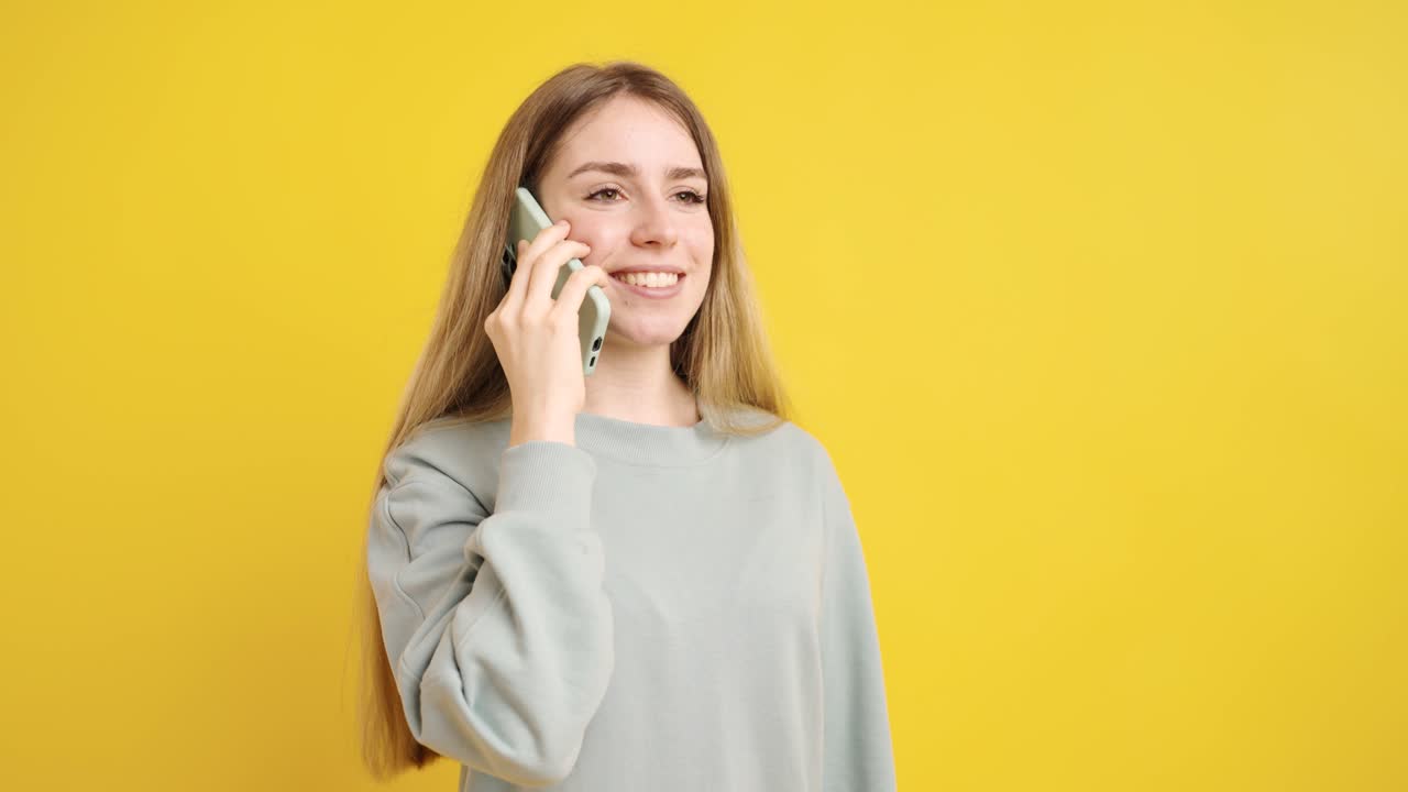 Young woman talking on mobile phone on yellow background