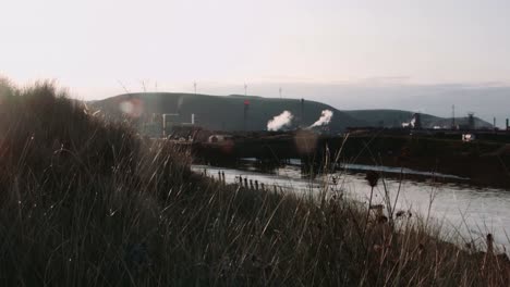 Cinematic-Sunrise-Reveal-of-Steelworks-Industrial-Plant-with-Wind-Turbines-on-Horizon