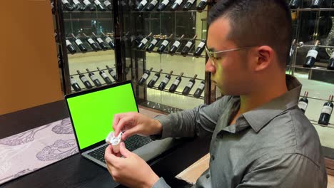 riqueza hombre asiático del milenio con auriculares asintiendo a la música frente a la pantalla verde de la computadora portátil
