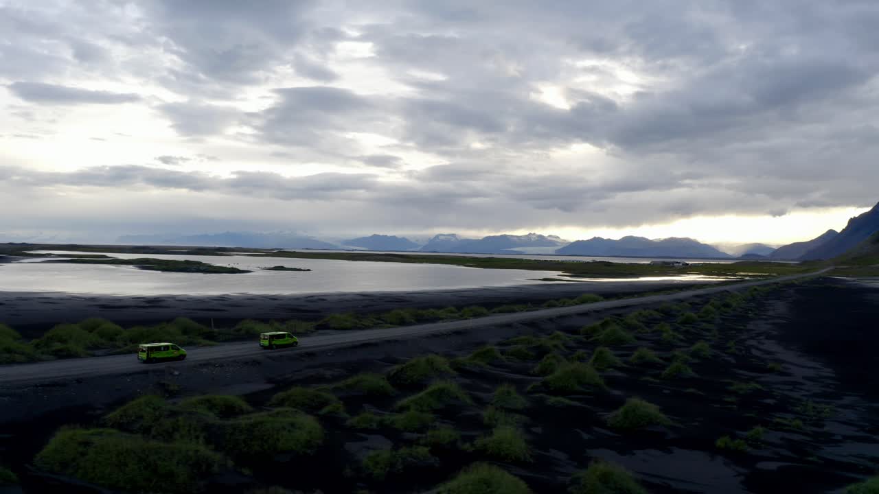 tomada de aviones no tripulados de coches que conducen a través del paisaje dramático de las montañas de vestrahorn y la playa bajo un cielo nublado