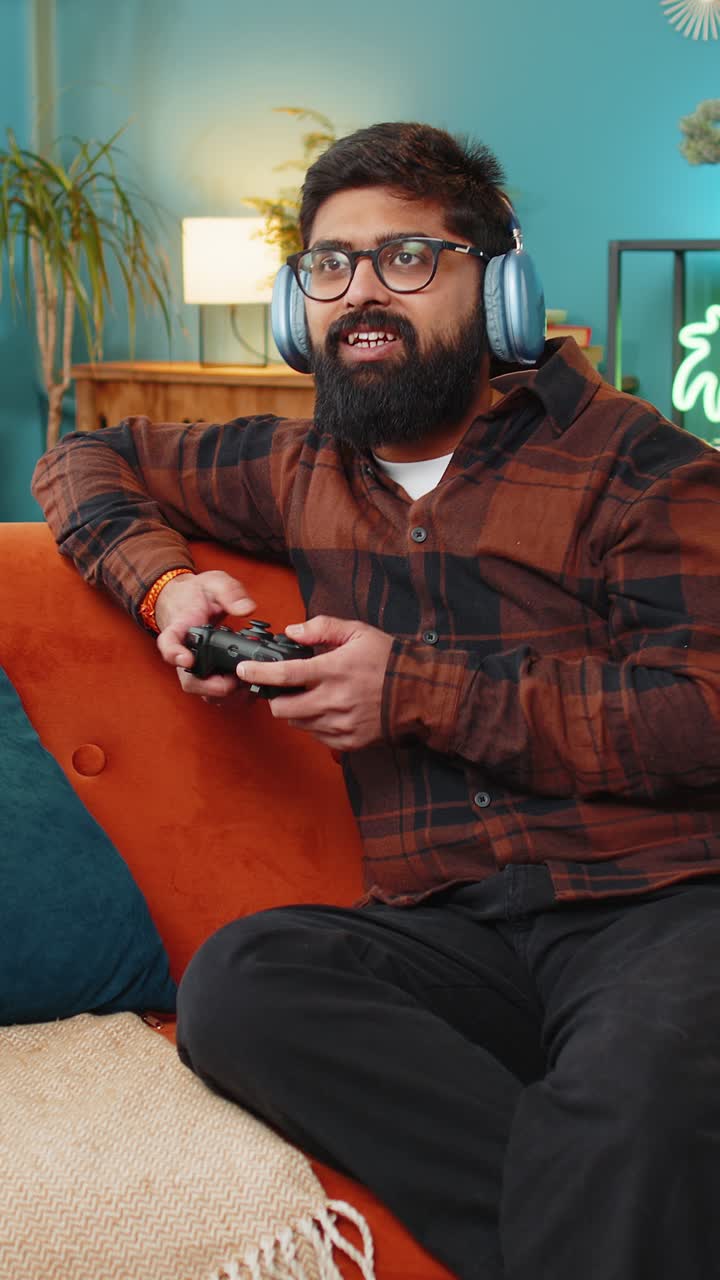 Indian young man using joystick controller playing video console game online game on home sofa