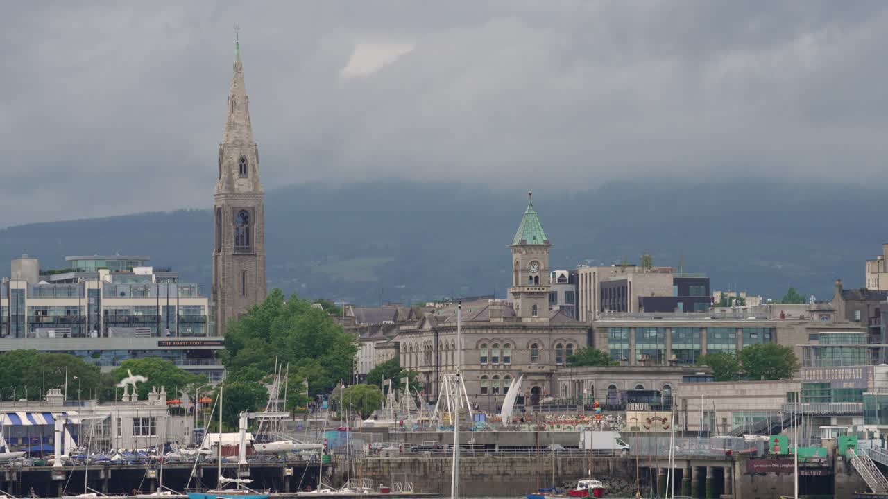 A scenic view of the historic harbor town of Cobh, County Cork, Ireland. The iconic spire of St. Colman's Cathedral dominates the skyline, with boats filling the marina below