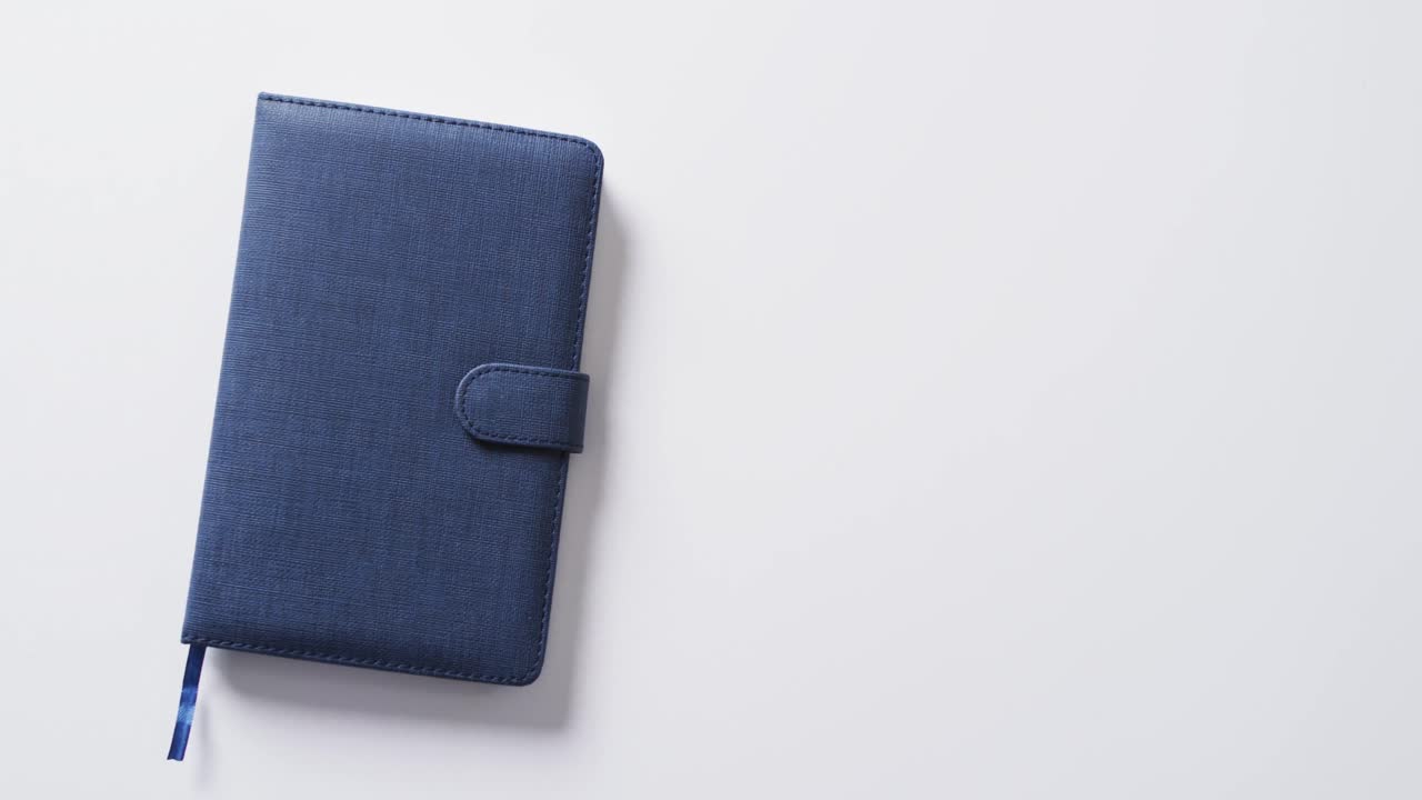Close up of closed blue notebook with copy space on white background in slow motion