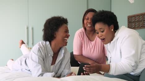 laughing together, african american women using smartphone on bed at home