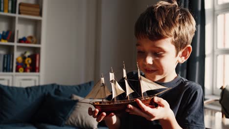 young boy holding a scale model of a galleon in his hands, admiring it, in the living room of his house, with some toys on a shelf in the background