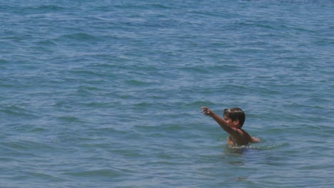 Medium,-follow-pan,-slow-motion-100fps-footage-of-8-years-old-caucasian-boy,-swimming-at-crystal-clear-blue-waters